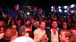 Eine große Menge an Menschen wartet auf die Ergebnisse der Wahl. Im Hintergrund weht die niederlänsche Flagge