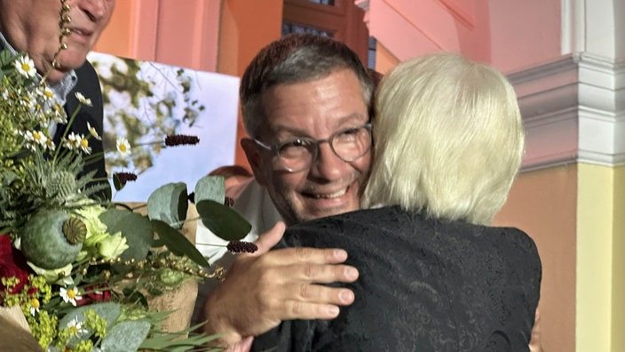Oberbürgermeister-Kandidat Marc Herter wird umarmt. Neben ihm befindet sich ein Strauß Blumen.