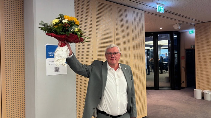 Das Bild zeigt Sebastian Schuster, der einen Blumenstrauß hochhält.