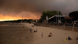 Frankreich, in der Nähe von Bordeaux: Menschen am Strand Andernos-Les-Bains während eines Waldbrands nachdem ein Teil der umliegenden Gegend evakuiert wurde
