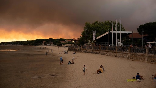 Frankreich, in der Nähe von Bordeaux: Menschen am Strand Andernos-Les-Bains während eines Waldbrands nachdem ein Teil der umliegenden Gegend evakuiert wurde