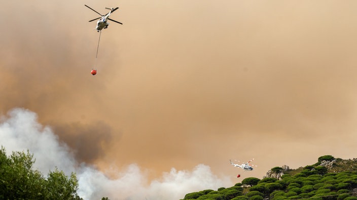 Löschhubschrauber fliegen über ein brennendes Waldstück bei Tarifa, Spanien