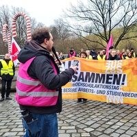 Auf einem Platz haben sich mehrere Menschen mit Bannern für einen Warnstreik versammelt