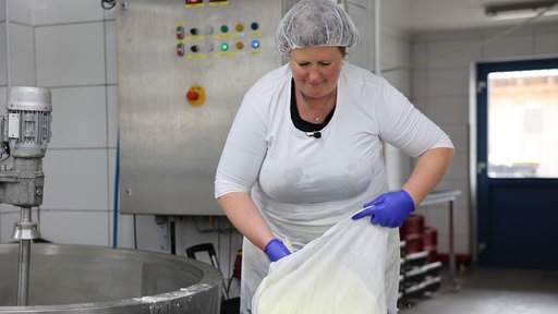 Eine Frau macht Frischkäse in der Produktionshalle.
