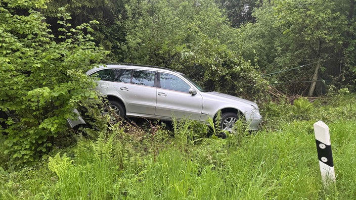Ein silberner Mercedes liegt mit Totalschaden im Graben. 