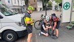 Drei Männer in Fahrradkleidung wechseln einen Fahrradreifen.