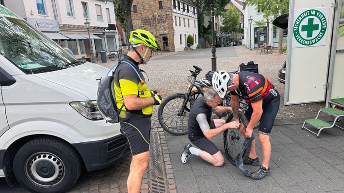 Drei Männer in Fahrradkleidung wechseln einen Fahrradreifen.