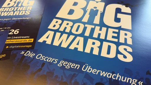 Mehrere blau gestaltete Plakate der Big Brother Awards liegen nebeneinander.