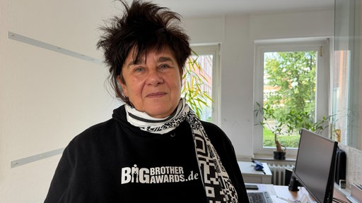 Jurymitglied Rena Tangens steht in einem Büro und trägt einen schwarzen Pullover der Big Brother Awards.