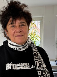 Jurymitglied Rena Tangens steht in einem Büro und trägt einen schwarzen Pullover der Big Brother Awards.