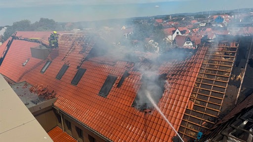 Rauch steigt aus dem beschädigten Dach der Michaelsschule in Paderborn auf, während die Feuerwehr den Brand bekämpft.