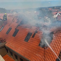 Rauch steigt aus dem beschädigten Dach der Michaelsschule in Paderborn auf, während die Feuerwehr den Brand bekämpft.