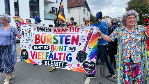 Menschen in Oma-Kostümen halten ein Banner mit Schriftzug hoch