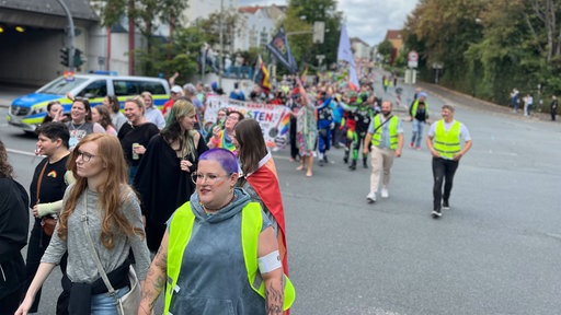 Menschen gehen reihenweise mit Bannern und Flaggen mit dem Queer-Regenbogen Symbol