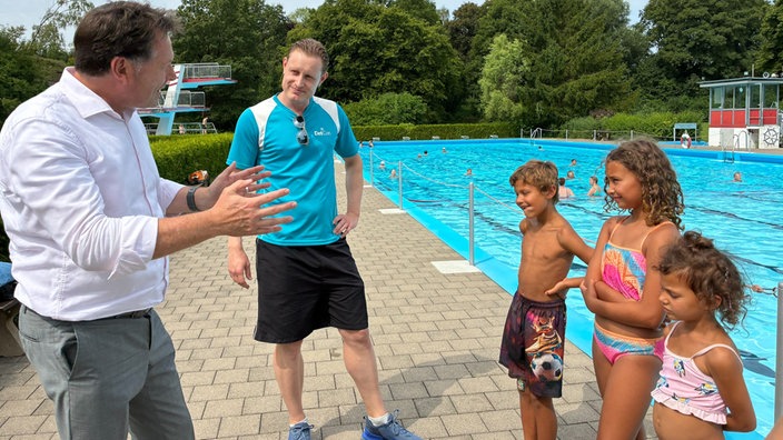 Drei Kinder sprechen in einem Freibad mit zwei Erwachsenen.