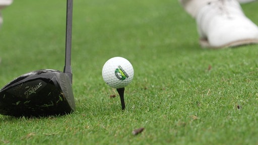 Ein Schläger vor einem Golfball, der auf einem Tee liegt.