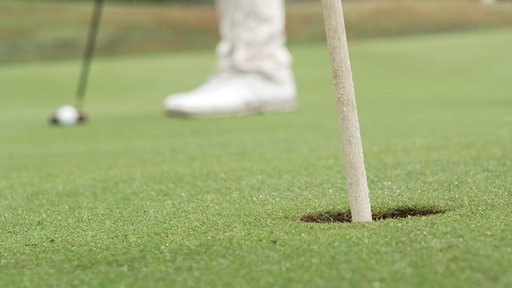 Ein Golfspieler will den Ball ins Loch schießen.