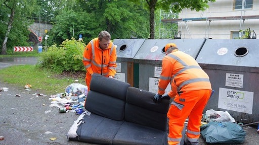 Zwei Männer der Stadtreinigung verladen ein Sofa.