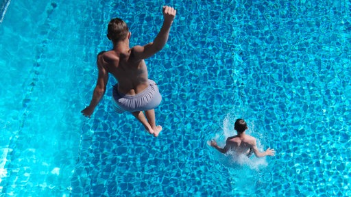 Personen springen von einem Sprungturm ins Wasser.