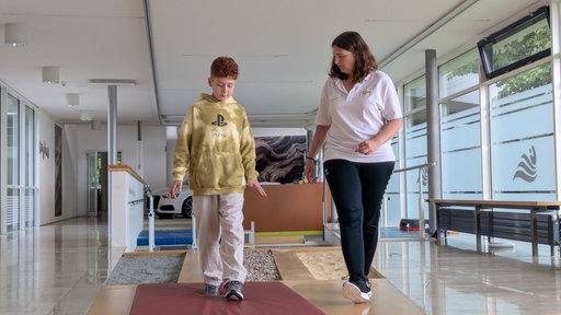 Ein Junge und eine Physiotherapeuthin absolvieren zusammen eine Übung.