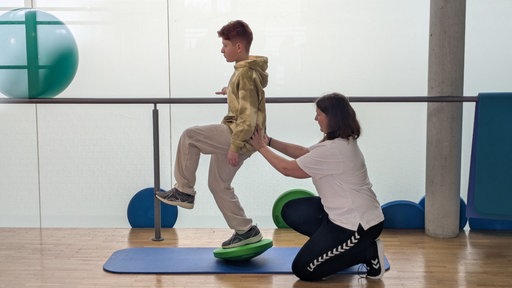Ein Junge und eine Physiotherapeuthin absolvieren zusammen eine Übung.