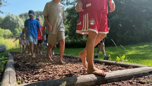 Kinder laufen über den Barfußpfad mit Rindenmulch.