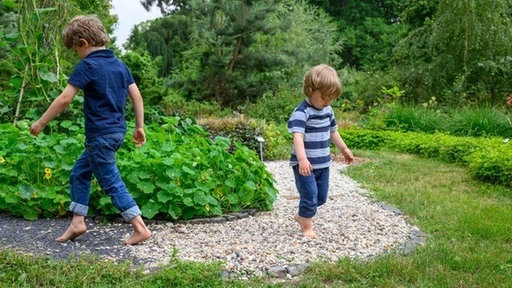 Zwei Kinder gehen Barfuß über einen Kieselweg