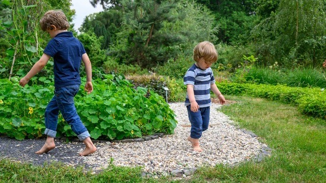 Zwei Kinder gehen Barfuß über einen Kieselweg