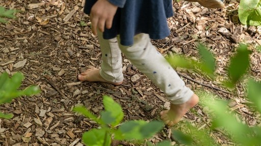 Kind geht Barfuß über einen Weg aus grober Holzspähne