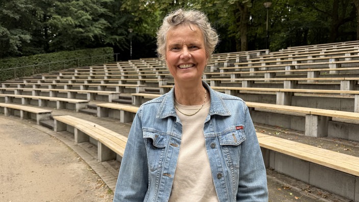 Eine Frau lächelt vor einer Freilichtbühne in die Kamera.