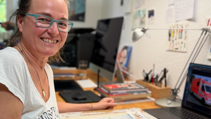 Brigitte Kuka schaut in die Kamera und sitzt an einem Schreibtisch.