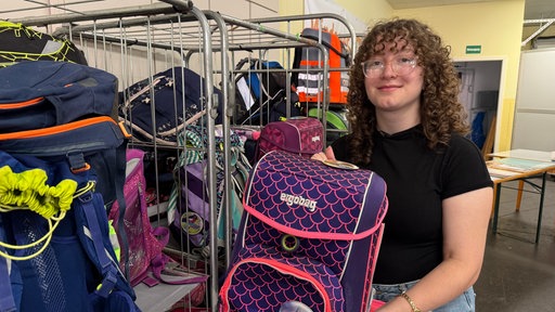 Eine Frau hält einen lila-pinken Schulranzen in die Kamera.