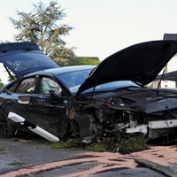 Ein stark beschädigtes schwarzes Auto steht mit geöffneter Motorhaube und Heckklappe am Straßenrand.