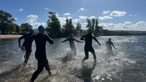Mehrere Triathletinnen und Triathleten laufen vom Ufer in einen See.