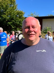 Ein Mann in einem dunkelblauen T-Shirt steht auf einer Wiese.