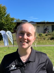 Eine Frau in einem schwarzen Poloshirt steht auf einer Wiese.