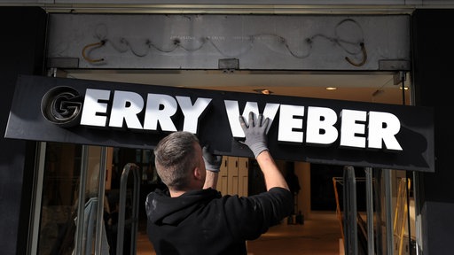 Ein Monteur hängt ein Schild mit dem Schriftzug "Gerry Weber" an einer Filiale der Modemarke ab.