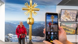Frau lässt sich vor dem zweiten Gipfelkreuz auf der Zugspitze fotografieren 