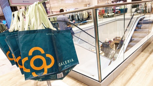 Taschen mit dem Firmen-Logo von Galeria hängen in einer Filiale
