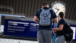 Reisende stehen vor einem Monitor auf einem Bahnsteig in Düsseldorf