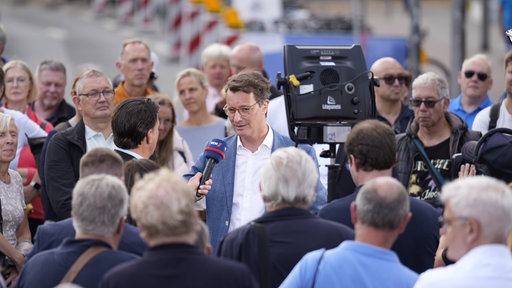 Hendrik Wüst steht in einer Menschenmenge und wird interviewt
