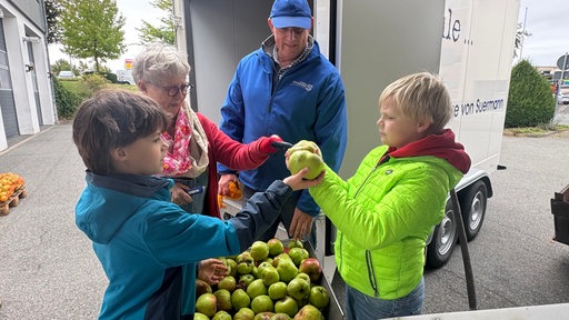 Kinder und Erwachsene begutachten Äpfel.