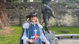 Ein Musketier-Darteller in Kostüm steht vor der d'Artagnian-Statue in Maastricht