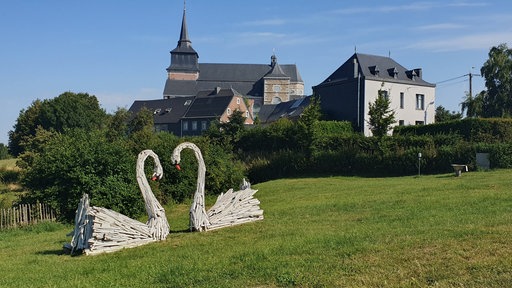 Naherholungspark Pré Desonay in Clermont-sur-Berwinne mit Schwanskulpturen und im Hintergrund der Kirche