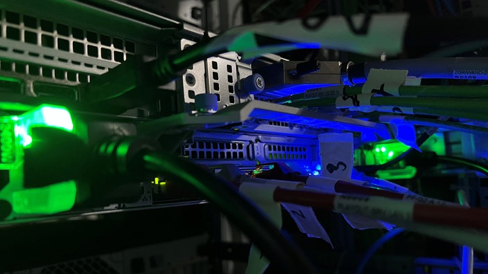 Das Bild zeigt die Nahaufnahme von Kabeln und Eingängen sowie blaue und grüne Lichter an den Apparaturen.
