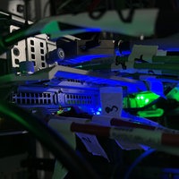 Das Bild zeigt die Nahaufnahme von Kabeln und Eingängen sowie blaue und grüne Lichter an den Apparaturen.