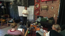 Zwei Mädchen sitzen auf Sesseln, ein Junge steht zwischen Flipcharts