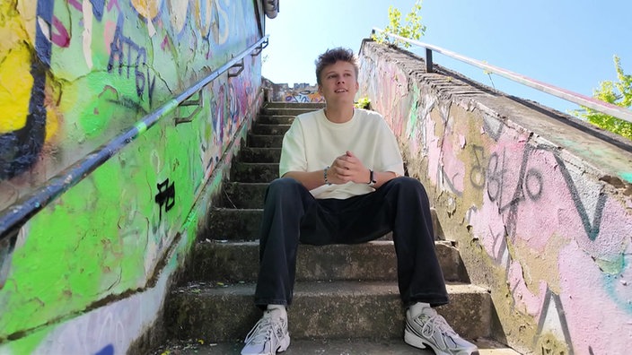 Ein Jugendlicher sitzt auf einer mit Grafitti besprühten Außentreppe