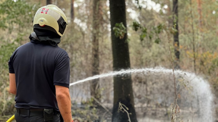 Eine Person mit Helm bei den Löscharbeiten im Wald