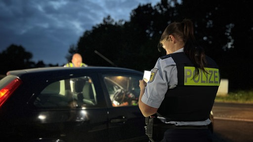 Zwei Polizisten kontollieren den Ausweis eines Autofahrers